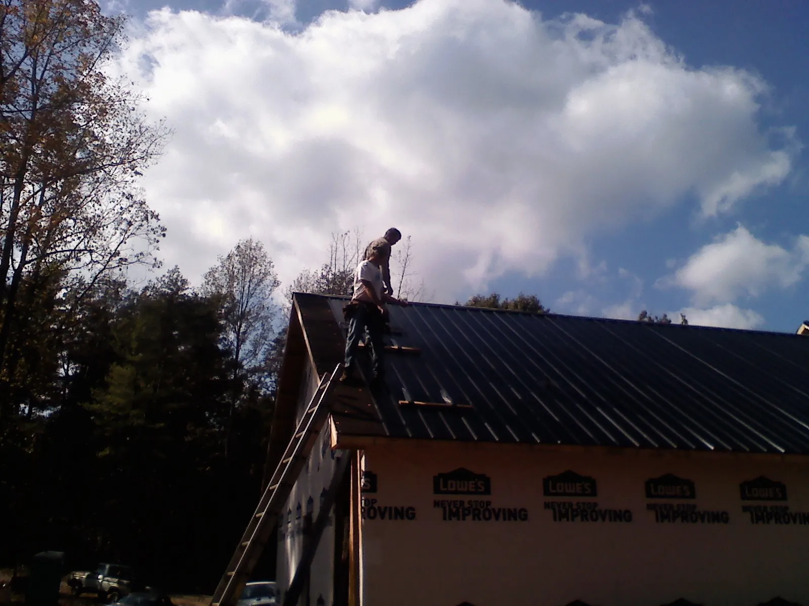 Roofer fastening dark metal panels high against a cloudy sky in Port Orchard