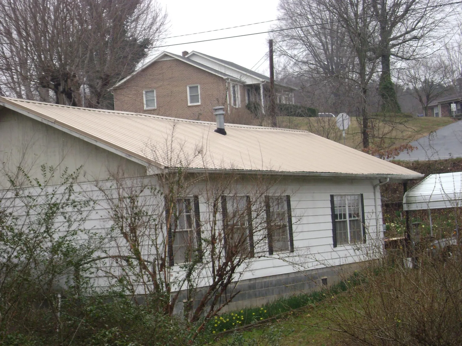 Tan metal roof on a white sided house set into a hillside — Commercial Roofing by Roofing Brothers in Port Orchard